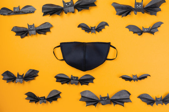 Reusable black anti-virus mask surrounded by paper bats. Orange background. Flat lay. The concept of protection from the virus during Halloween