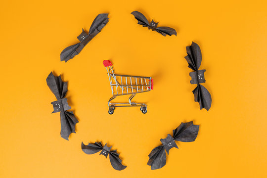 The customer's toy cart is located in a circle of bats made of paper. Orange background. Copy space. Flat lay. The concept of Halloween and holiday shopping