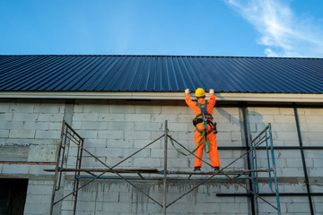 Roofer worker in protective uniform wear and safety line working install new roof at construction site.