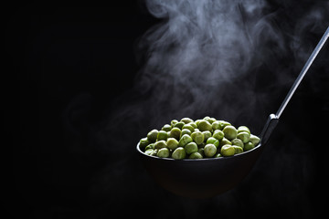 Cooked peas in a kitchen ladle with rising steam