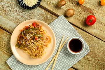 Funchoza with vegetables and mushrooms in a plate on a napkin near sticks and soy sauce tomatoes...