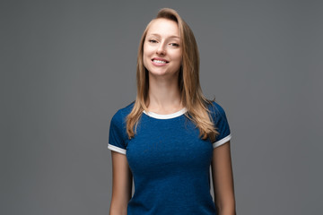 Obraz premium Studio shot of pretty female with blonde straight hair, broad smile, wears blue t shirt, tilts head and looks with joy