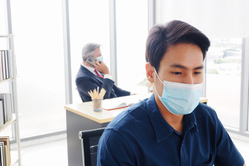 Fototapeta na wymiar Young Asian male wearing face mask working in the office to prevent the Covid19 virus for good health and hygiene at workplace and social distancing concept