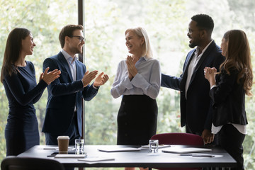 Diverse millennial corporate staff greeting aged woman colleague for her contribution to project...