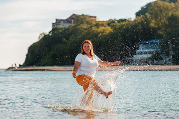 Summer vacation. A happy woman walks along the seashore, splashing and having fun. Copy space