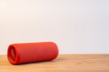 Red bluetooth speaker on wooden table with white background. Space for texture.