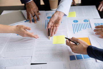 Close up of diverse businesspeople group discussing charts and graphs on meeting, multiethnic team of corporate managers or employees analyzing information materials hardcopy in office together