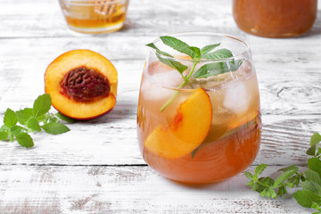 Iced tea with nectarines topped with mint in glass on the white table. Summer drink