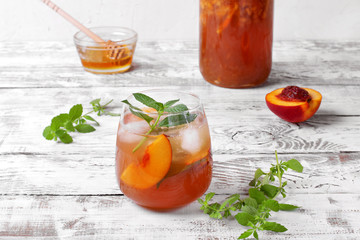 Iced tea with nectarines topped with mint in glass on the white table. Summer drink
