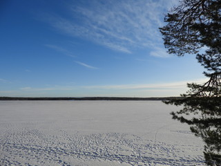 Large frozen winter lake covered with snow and footprints, against a blue sky