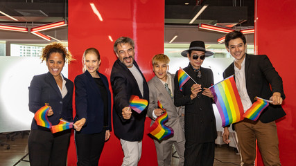 Business office workers from different ethnicities express support for self determination in LGBT. Business people showing LGBT flags in an office
