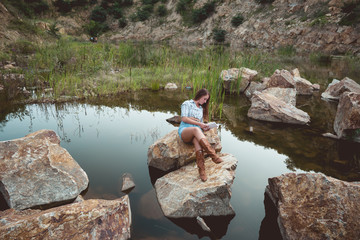 Young woman reading a book by the lake .One female enjoying relaxing and reading book by a mountain lake