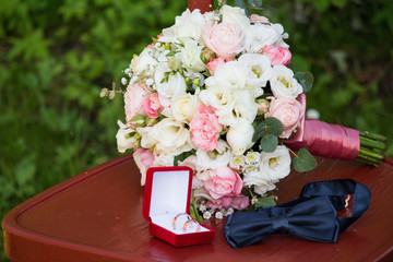 Bride's wedding bouquet of white and pink flowers. Blue bow tie next to gold wedding rings in a red...