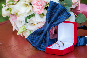 Bride's wedding bouquet of white and pink flowers. Blue bow tie next to gold wedding rings in a red box. White and pink roses.