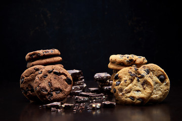 White and brown cookies on dark background.Freshly  baked chocolate chip cookies with place for text. Traditional homemade cookies.Closeup of a group of assorted cookies.Broken chocolate pieces .