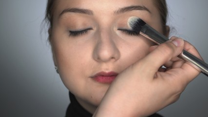 Makeup artist making professional make-up for young woman in beauty studio. Make up Artist applies blush with brush on eyelid