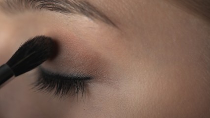 Makeup artist making professional make-up for young woman in beauty studio. Make up Artist applies blush with brush on eyelid
