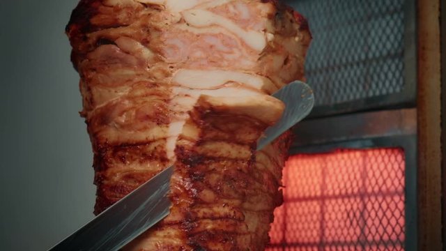 The knife slices the meat on a shawarma skewer.