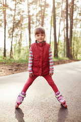 Fototapeta premium Cute girl posing on road in forest, wearing casual shirt and rolling skate, looking directly at camera, spending time in open air, being photographed by mother.
