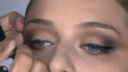 Macro shot of makeup artist making professional make-up for young woman in beauty studio. Make up Artist draws arrows over eye, eyeliner