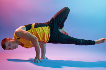Young man doing an asana, standing on hands, practicing body balance, wearing sports wears, doing yoga exercises isolated over neon wall, sportsman working out.