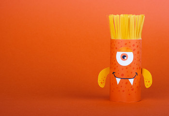 a brown scary monster made from a roll of toilet paper on orange background