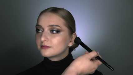 Makeup artist making professional make-up for young woman in beauty studio. Make up Artist applies blush with a big brush