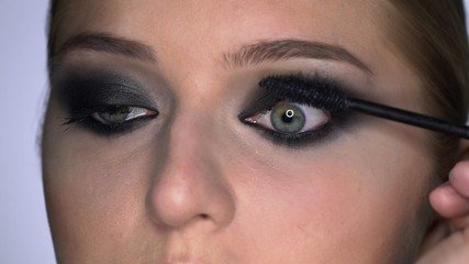 Naklejka premium Side view of makeup artist making professional make-up for young woman in beauty studio. Make up Artist paints eyelashes mascara