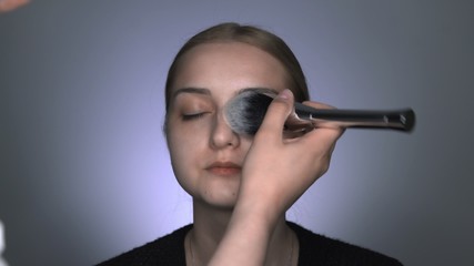 Fototapeta premium Makeup artist making professional make-up for young woman in beauty studio. Make up Artist applies powder with a big brush