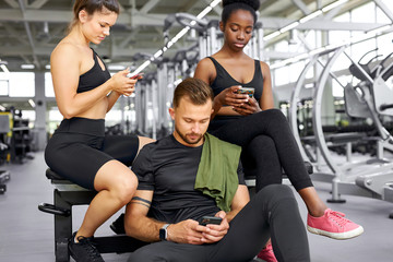 Fototapeta na wymiar portrait of tired diverse fit people enjoying time after sport exercises, african and caucasian team sit together in gym, using smartphone