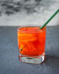 Orange cocktail with tropical fruits in square glass cup with paper cocktail tube