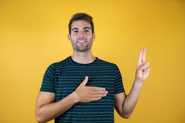 Young handsome man smiling swearing with hand on chest and fingers up, making a loyalty promise oath