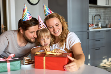 little caucasian girl in anticipation of receiving, unpacking gifts from parents. adorable happy girl celebrate birthday at home with family