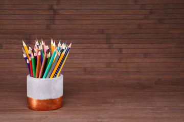 Colored pencils in a plaster cup on a natural, mahogany background made of wooden boards. Website concept, school related topic.