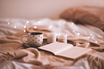 Cup of coffee with open book and candles in bed closeup. Autumn season. Good morning. Selective focus.