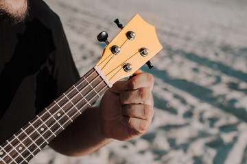 Closeup of a person tuning the ukulele at a beach under the sunlight