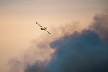 Amphibious water bomber airplane in flight at sunset, smoke from a forest fire, in France.