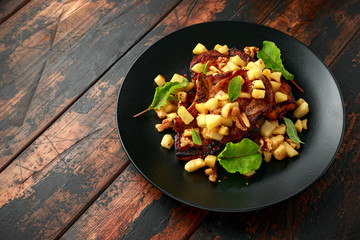Roasted Pork chops with caramelized apples, walnuts and sage in black plate on wooden table