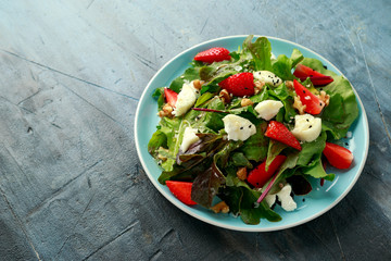 Goats cheese and strawberry summer salad served with nigella and sesame seeds drizzled with runny honey