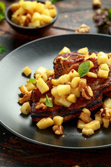Roasted Pork chops with caramelized apples, walnuts and sage in black plate on wooden table