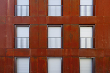 Fototapeta na wymiar Outdoor exterior front view of modern building with typical rectangular windows, balcony, railing and shutter curtain windows on symmetric pattern and rust copper facade..