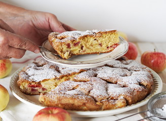 Senior woman is homemade cakes. Charlotte making process. An elderly woman is hands sprinkle icing sugar on a pie with apples and plums.