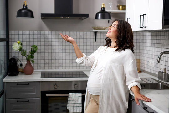 Inspired Happy Woman Expecting Baby, Stand In The Kitchen Alone, Smiling And Looking Away