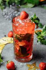 Strawberry Mojito. Cold summer mojito cocktail with strawberries, mint, lemon and ice in a glass on a table. on a dark background