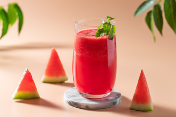 summer watermelon smoothie in a glass and watermelon slices and green leaves in the background. healthy refreshing drink. beige background