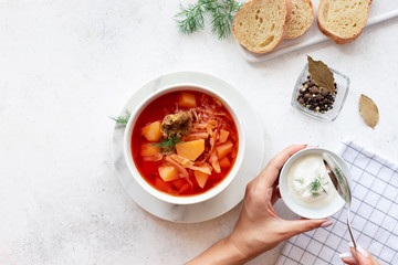 woman's hands put sour cream in a bowl with red borscht soup. Traditional Russian Ukrainian beet soup. top view. White background. copy space