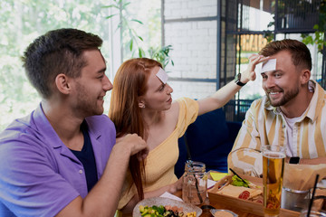 little sticker on the forehead. friends having fun in the restaurant, caucasian young people playing a hedbanz game, laugh