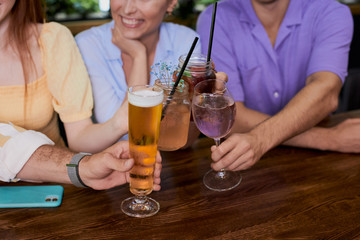 group of young people clink glasses with beverages in restaurant or bar, have a great time at weekends, some rest