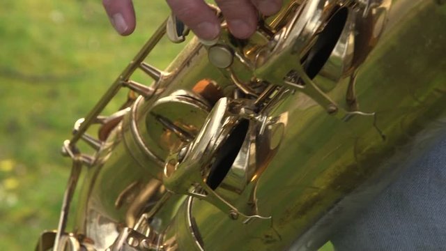 Close up of a baritone saxophone and the hand that is playing it outdoors
