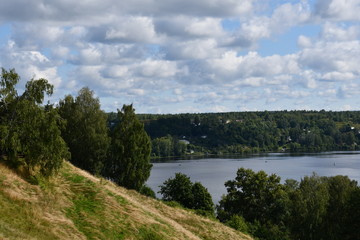 Obraz premium A picturesque view of a large river with green banks. Beautiful clouds are reflected in the water.